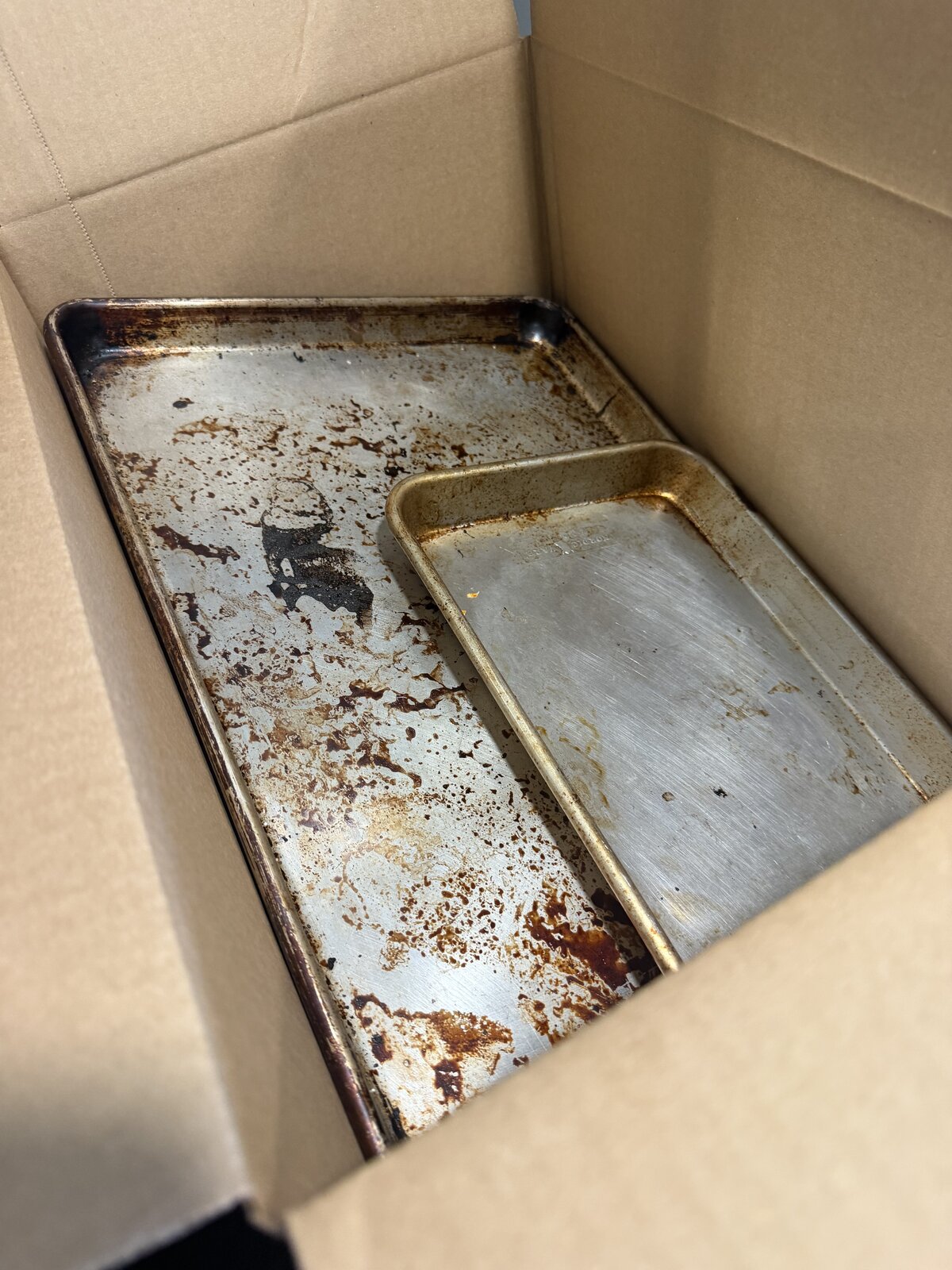 Two baking sheet pans laid flat in the bottom of a small box