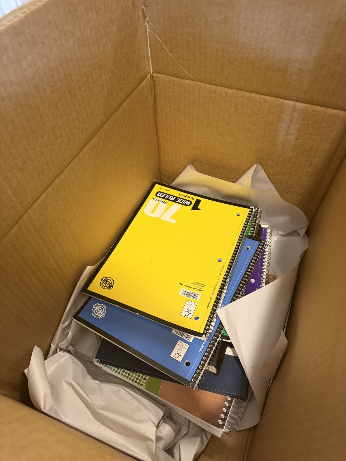 A handful of school notebooks and packing paper in a small box